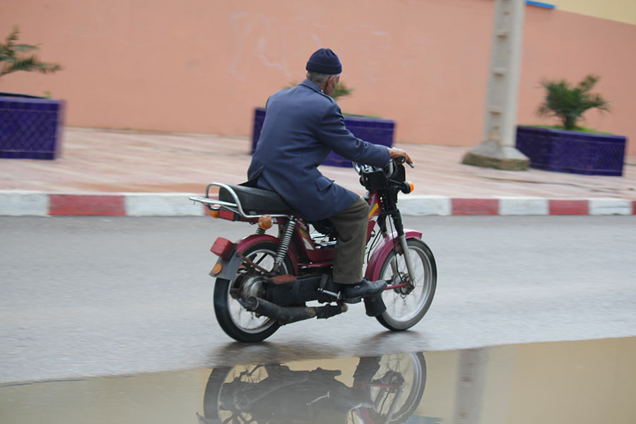 Vieil homme sur une motocyclette avec son reflet dans une flaque d'eau